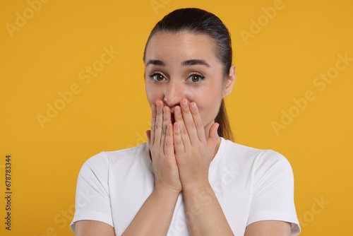 Embarrassed woman covering mouth with hands on orange background