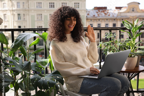 Beautiful young woman using laptop surrounded by green houseplants on balcony photo