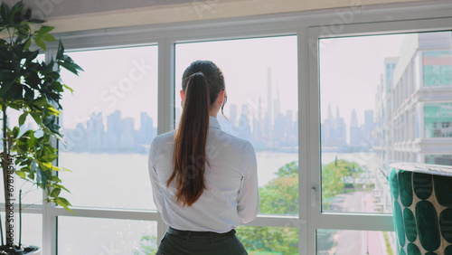 Back view of successful young Caucasian businesswoman approaching window in modern office looking at view using smartphone online. Beautiful elegant female worker in suit. Free Download Back view of successful young Caucasian businesswoman approaching window in modern office looking at view using smartphone online. Beautiful elegant female worker in suit. - GFXLoad