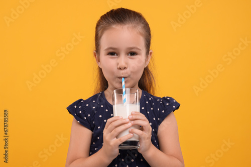 Cute girl drinking fresh milk from glass on orange background