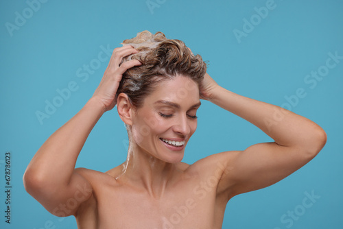 Beautiful happy woman washing hair on light blue background