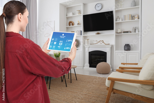 Woman using smart home control system via application on tablet indoors