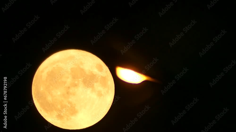 Night dark sky, orange full moon during moonrise and light of lamp - real time. Topics: electric light, electricity, energy, weather, atmosphere, space, astronomy, cosmos, dusk
