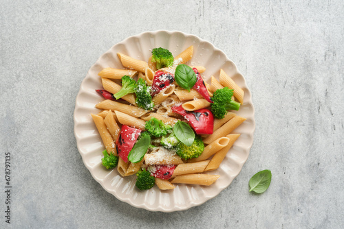 Wholegrain pasta penne with broccoli and red grilled bell pepper and on light grey slate, stone or concrete background. Vegan pasta. Traditional Italian cuisine. Flat lay. Copy space