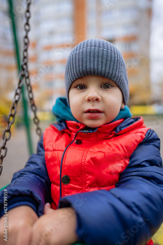 A Playful Moment in the Park. A little boy sitting on a swing with a hat on photo