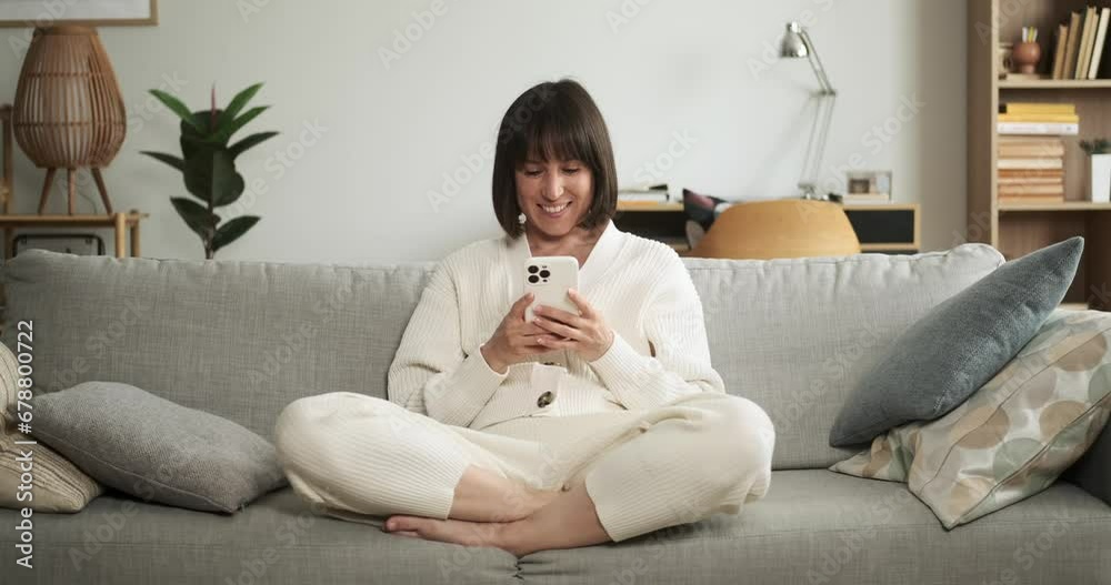 Cheerful woman sits on the living room couch, smiling as she engages in texting on phone. Her joyful expression captures the pleasantness of digital communication. Cheerful woman sits on the living room couch, smiling as she engages in texting on phone. Her joyful expression captures the pleasantness of digital communication.