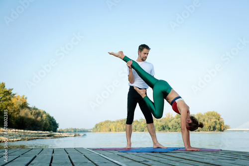Couple practicing yoga on wooden deck by the river