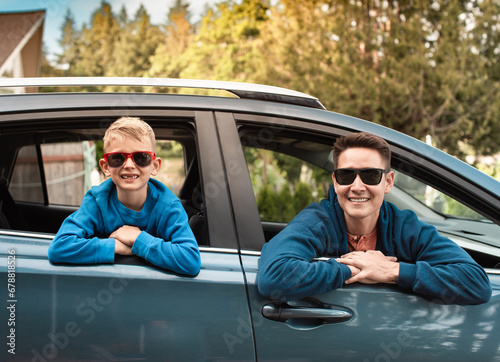 Happy smiling father and son portrait sitting in car looking out window ready for family roadtrip adventure. 