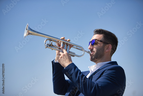 Young Hispanic man  wearing a jacket and sunglasses  playing a pretty  silvery trumpet outdoors. Concept  music  instruments  trumpet.