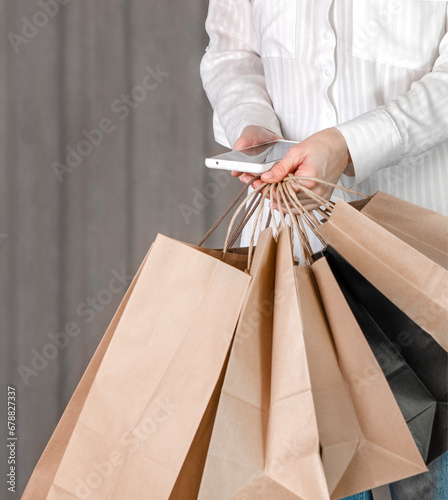 A girl in a white shirt and blue jeans holds craft paper bags and a phone in her hand. Shopping concept