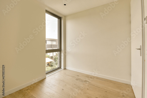 an empty room with wood floor and large window looking out onto the street below  there is a white door that leads to a
