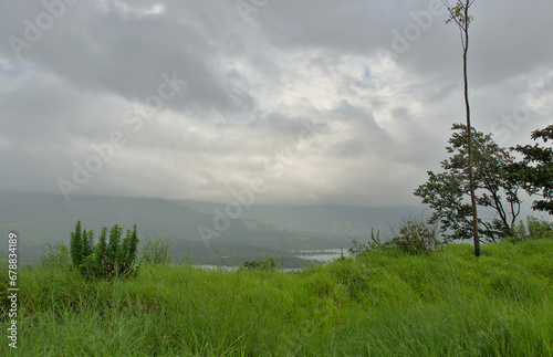 Panoramic view of lush green landscape and Sahyadri mountains with clouds in Tapola, a famous tourist place during monsoons in Maharashtra, India
