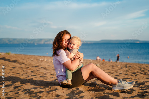 Young mother spends time with cute baby child toddler by the sea at sunset