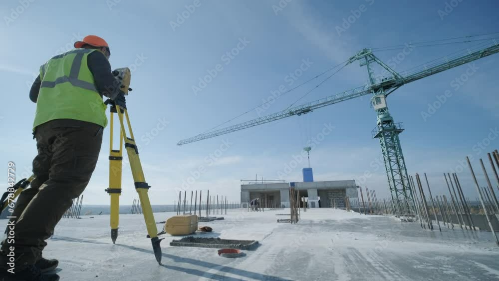 Geodetic works. Surveyor engineer in protective wear and red helmet using geodetic equipment at construction site. Professional equipment.