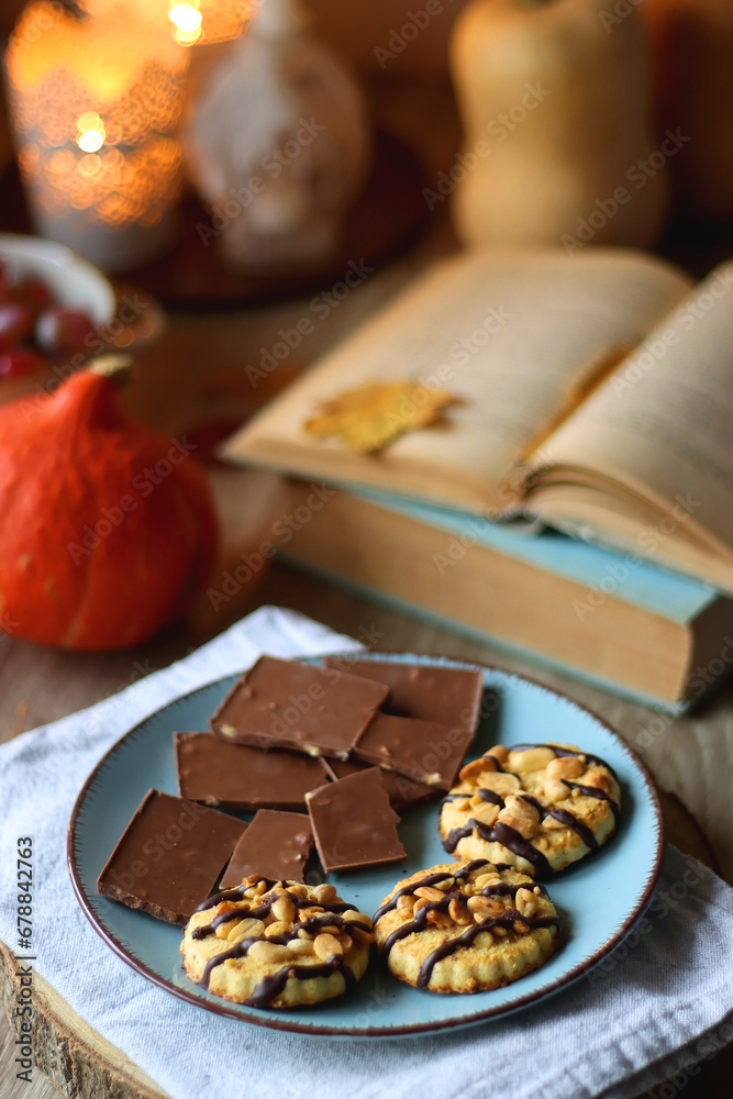 Cup of tea or coffee, plate with desserts, dried oranges, bowl of grapes, scented candles, vintage books, pumpkins and autumn leaves on the table. Autumnal hygge. Selective focus.