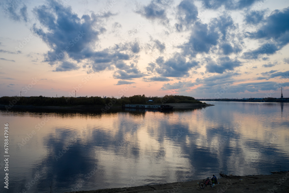 Sunset over the river. In the water surface mirrored clouds. Two fishermen are sitting on the shore, bicycles nearby. Silence and solitude. Shooting from a drone.