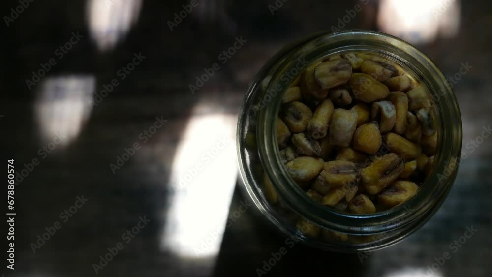 Roasted corn kernels on the table in the sun. A jar of roasted corn on the table, under random rays of sunlight. A pot of roasted corn on a wooden table. Roast corn on a cutting board. Roasted corns Roasted corn kernels on the table in the sun. A jar of roasted corn on the table, under random rays of sunlight. A pot of roasted corn on a wooden table. Roast corn on a cutting board. Roasted corns