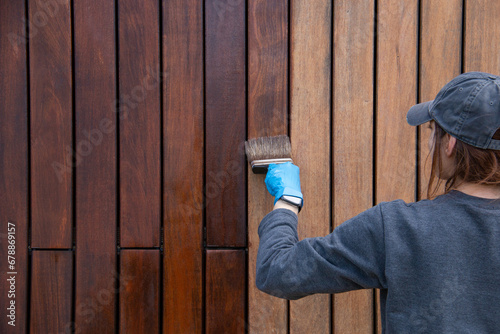 Handywoman applying protective varnish or paint with brush on wood fence wall cladding close up. Hardwood cladding house improvement diy concept