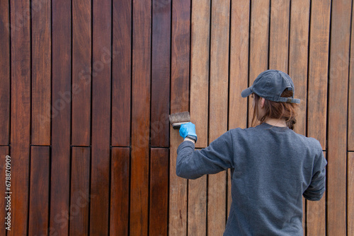 Woman applying protective varnish or paint on wooden house cladding