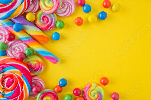 Various lollipops and round candy in bright and bold colours on a yellow background, with space for text