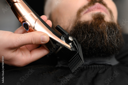 Cutting a gentlemans beard in a barbershop with a clipper. Shortening the length of the beard from the sides by the master for the client.