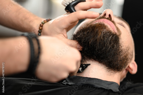 A barber in the salon trims the beard of a man with a trimmer in the neck area
