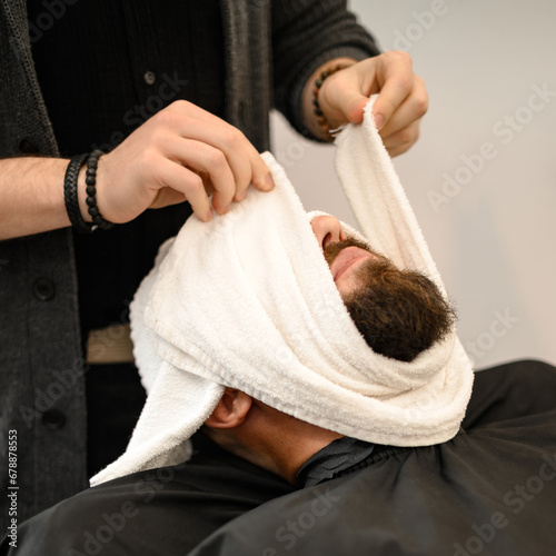 Konstfotografi The barber covers the client face with a hot wet towel to steam off the beard