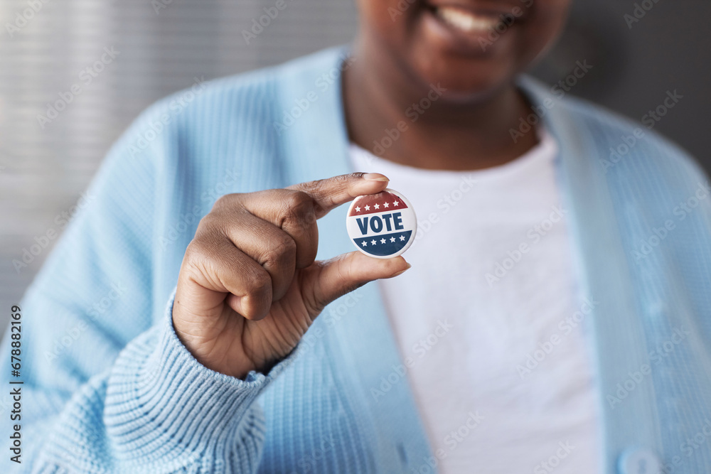 Focus on hand of young African American woman in casualwear holding small round vote badge while standing in front of camera - obrazy, fototapety, plakaty 