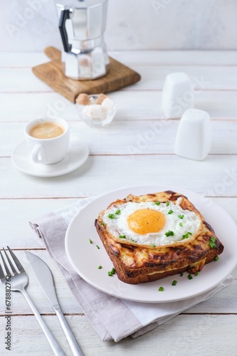 Hot croque madame sandwich with ham, cheese and fried egg on a white plate on a light wooden background. Sandwich recipes, hot breakfasts.