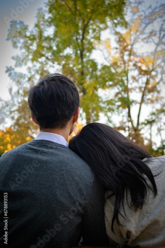 Vertical shot of a girl with her head on his boyfriend's shoulder in a park