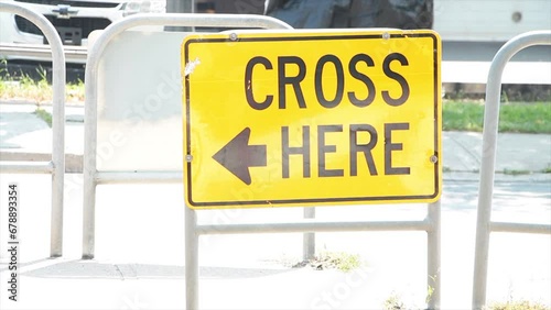 cross here with arrow writing caption text street road sign on island in middle of road in black on yellow with cars vehicles traffic passing behind and in front photo