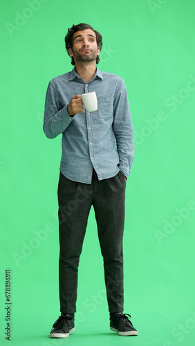young man in full growth. isolated on green background. holding a mug of coffee