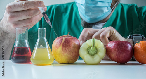 Biochemist working in farming laboratory analyzing gmo vegetable. Closeup of scientist biologist hands injecting organic apple with pesticides using medical syringe during microbiology experiment. photo