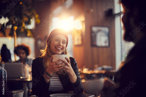 Smiling young woman holding coffee mug sitting with friend in cafe photo