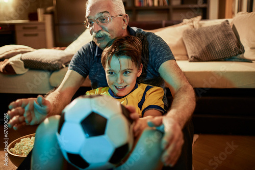 Young boy watching football game soccer match with grandfather at home photo