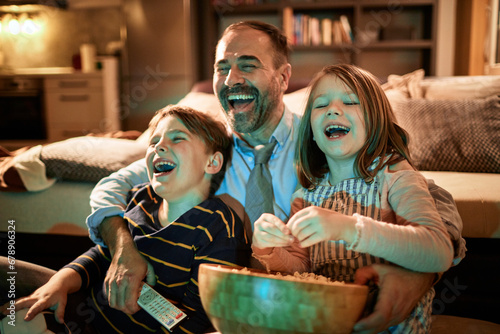 Father and children laughing during family movie night at home photo