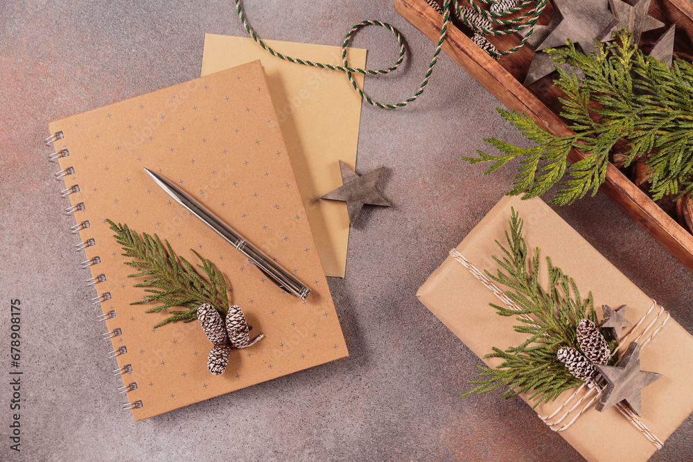 Winter holiday mood, Christmas, New Year composition on gray background. Notebook with envelope and pen, handmade gift box and Christmas wooden decor. Flat lay, top view