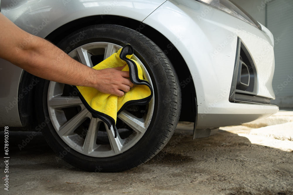 Obraz premium A Man Cleaning the Wheels of a Car with a Yellow Cloth. Car Detailing and Cleaning Concept with Space for Copy