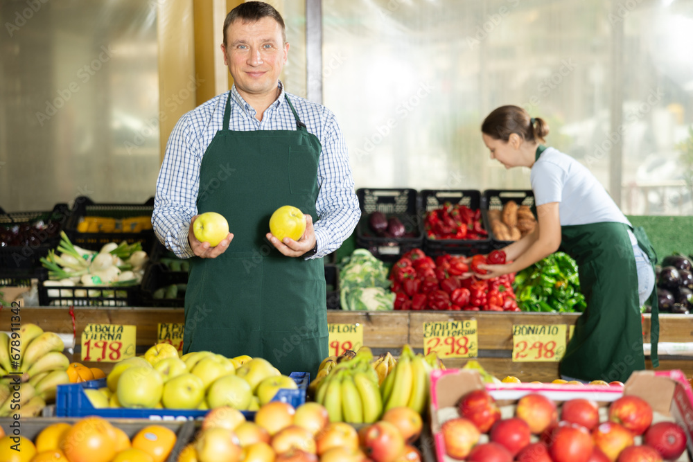 Man seller working in supermarket and lays out fresh apples on counter