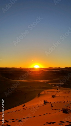 Vertical shot of dunes with footprints on the sand on the background of a golden sunset