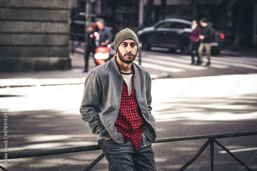 From below, young man leans on roadside barrier, urban style in Madrid's autumn.
