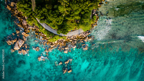 Aerial view Top down seashore. Beautiful azure sea surface with winding bike path in sunny day summer background Amazing seascape top view seacoast at Anse Severe Beach, La Digue Seychelles