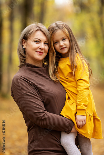 Beautiful mother and daughter walking in the park in autumn, portrait. Mom and daughter, family concept. A little girl in her mother's arms. Happy family on an autumn walk