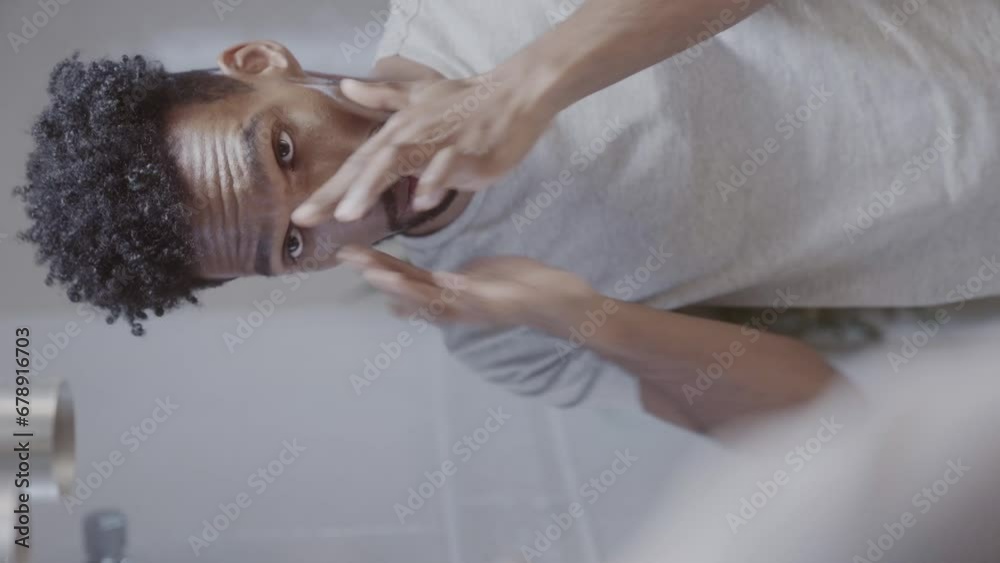 Homem negro olhando no espelho do banheiro durante sua rotina matinal em casa. Cinematico 4k. Video vertical.