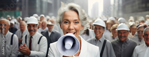 Labor International workers day. Senior woman speech a protest in a megaphone on city street. A crowd of old working men in rally. Pensioner yells into a bullhorn on people background. Female leader.
