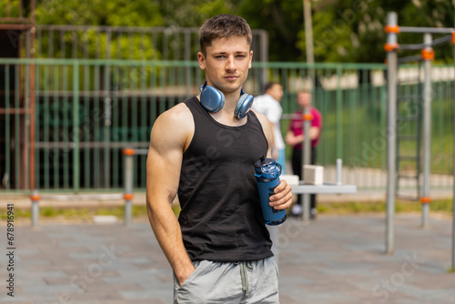 Portrait of athletic caucasian muscular man in sportswear holding drinking water bottle. Guy on playground before cardio workout exercises. Sports health fitness routine. Motivation. Outdoors gym