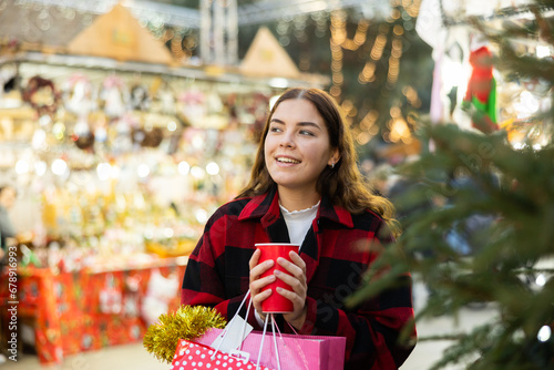 Girl holding a paper cup with mulled wine while enjoying a walk through the traditional city street fair on Christmas Eve