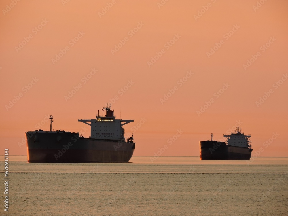 two large cargo ships sitting in the ocean during sunset, just before sunset