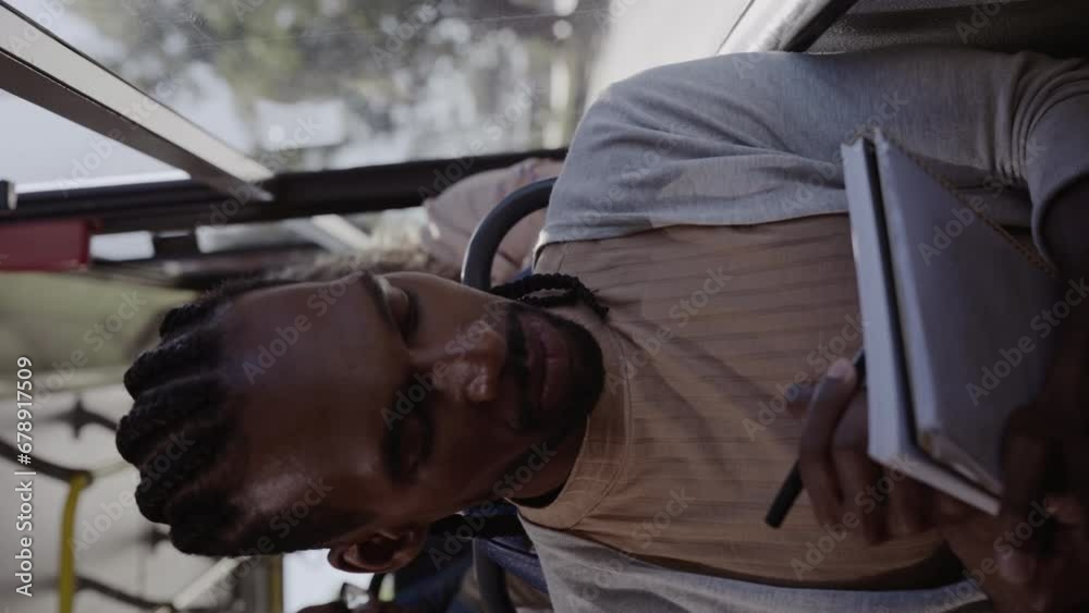 Homem negro jovem escrevendo em um caderno durante trajeto de onibus. Cinematico 4k. Video vertical.