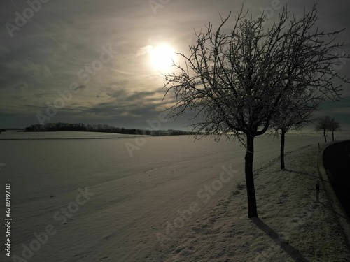 Scenic view of a winter landscape in a rural area with the sun shining in the cloudy sky